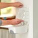 A person putting a plastic bag into a white Noble Chemical hand soap dispenser.