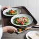 A person holding a Cambro non-skid serving tray with a plate of salad with carrots and mushrooms.