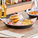 A black plastic round food basket filled with a cheeseburger and french fries on a table.