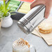 A hand using a Choice stainless steel shaker to sprinkle a drink.
