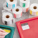 A hand using a roll of Noble Products Day of the Week labels to put a white label on a tray.