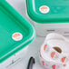 A green plastic container with a roll of Noble Products Saturday day of the week stickers on a table.