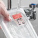A dissolvable day of the week label being washed off a food storage container under running water.