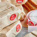 A stack of brown paper bags with a roll of white and red Point Plus Turkey & Cheese labels.