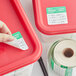 A hand using a Noble Products Friday food label to label a red container.