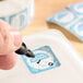 A dissolvable Monday day of the week clock label being written on with a marker, attached to a food container.
