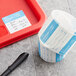 A roll of Noble Products Monday dissolvable food labeling stickers on a grey surface with a black pen.