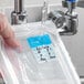 A plastic container with a dissolvable day of the week label being rinsed under running water.