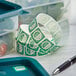 A roll of Noble Products Friday dissolvable day of the week stickers next to a green container and a pen.