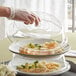 A person putting food into a stack of Choice clear polycarbonate plate covers.