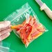 A gloved hand using a knife to open a Clear Line plastic food bag filled with red peppers.