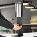 A person using a Lavex stainless steel automatic liquid sanitizing station.