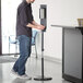 A man using a Lavex stainless steel automatic hand sanitizer station.