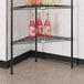 A Regency black metal triangle shelf with bottles of liquid on it.