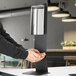 A person using a Lavex stainless steel automatic liquid soap dispenser on a counter.