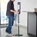 A man using a Lavex white metal automatic liquid sanitizing station.