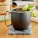 An Acopa Black Moscow Mule Mug filled with ice and lime slices on a marble coaster.