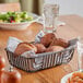 A rectangular black wire basket filled with bread on a table.