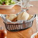 An Acopa black wire basket with rolls on a table.