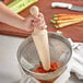 A person holding a Choice wooden pestle over a bowl of vegetables.