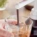 A hand pouring Capora Chocolate Flavoring Sauce into a glass of ice.