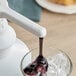 A person pouring Capora Blueberry flavoring sauce into a glass with ice.