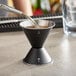 A metal jigger with liquid being poured into it.