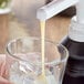 A hand pours Capora White Chocolate Flavoring Sauce into a glass of ice.