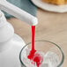 A white dispenser with Capora Strawberry Flavoring Sauce pouring red liquid into a glass with ice.