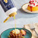 A white chocolate syrup being poured onto a cupcake on a blue plate.