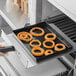 A hand holding a Baker's Mark non-stick tray with fried onion rings.