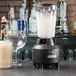 A Hamilton Beach commercial blender with a glass and a bottle of liquid on a bar counter.