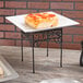 A square pizza on a black metal American Metalcraft pizza stand on a table.