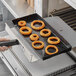 A hand holding a Baker's Mark solid non-stick pan of fried onion rings.