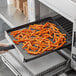 A person holding a Baker's Mark mesh basket of fries in a commercial oven.