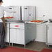 A commercial flat bottom fryer with trays of donuts being prepared in a kitchen setting.