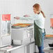 A woman using a Carnival King countertop fryer to make funnel cakes in a commercial kitchen.