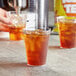 A hand pouring DominAde iced tea into a glass on a table.