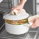 A person using a white Valor enameled cast iron Dutch oven to cook on a stove.