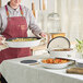 A woman in an apron holding a white Valor enameled cast iron skillet full of food.