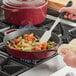 A person cooking potatoes and onions in a red Valor enameled cast iron skillet on a stove.