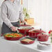 A woman holding a red Valor enameled cast iron Dutch oven with food in it.