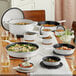 A table with a Valor Arctic White enameled cast iron pot with a lid on it and a white bowl of food.