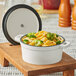 A Valor Arctic White enameled cast iron pot with broccoli and cheese on a wood surface.