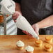 A person using a Choice plastic coated canvas pastry bag to pipe white frosting onto cupcakes.