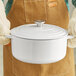A person wearing gloves holding a white Valor enameled cast iron dutch oven with a lid.