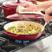 A person cooking food in a red Valor enameled cast iron pot on a stove.