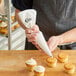 A person holding a Choice plastic coated canvas pastry bag over a cupcake with white frosting.