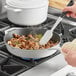 A person using a Valor Arctic White Enameled Cast Iron Skillet to cook mushrooms and herbs on a stove.