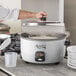 A person cooking rice in an Avantco rice cooker using a white pot with a lid.